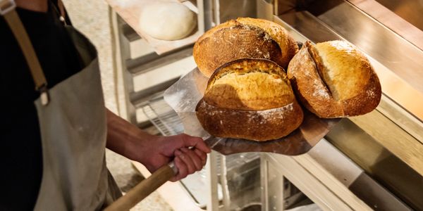 Baker removing freshly baked bread from oven using a peel.