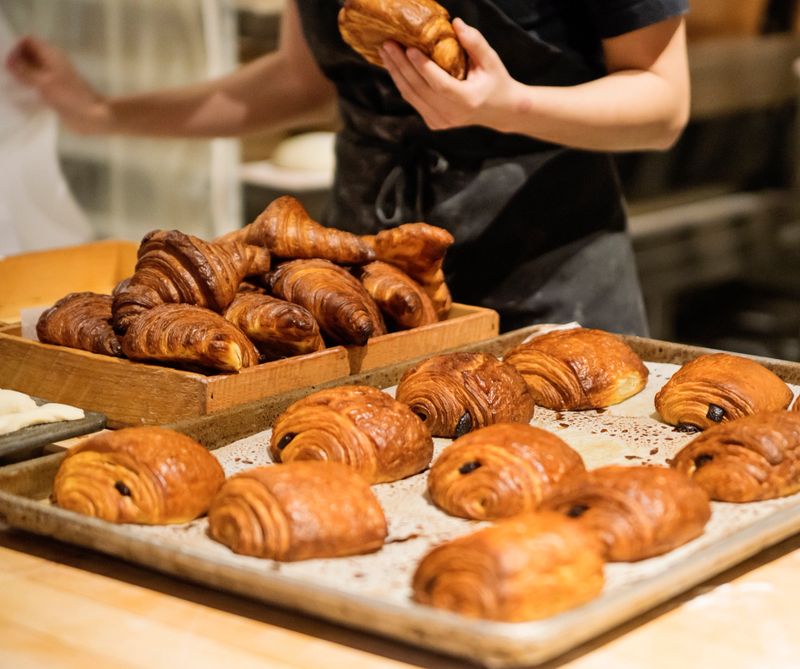 Morning routine for millennial latino bread maker displaying freshly made chocolate croissants on trays in very early morning. Horizontal close-up shot with copy space.