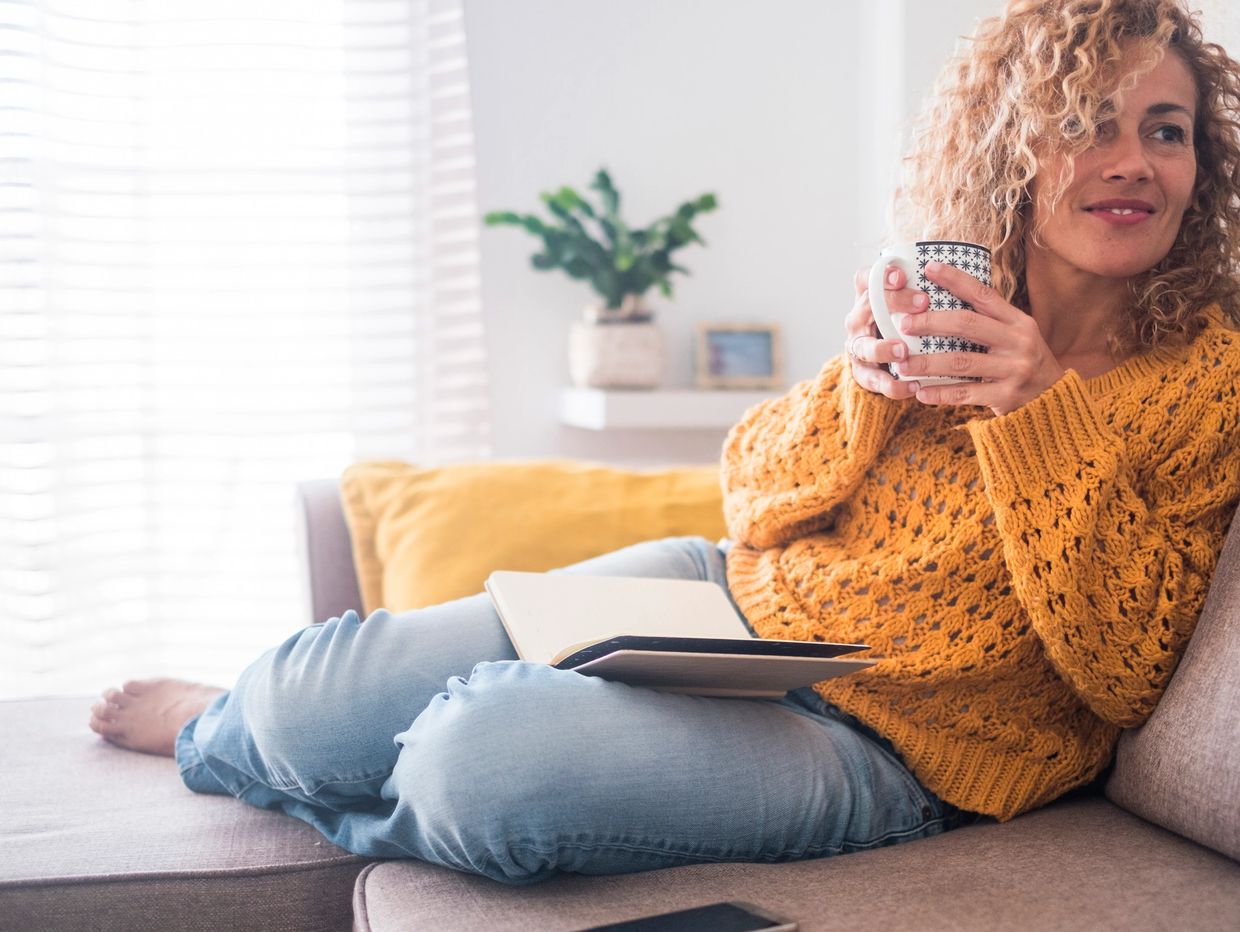Woman relaxing on couch with a cup and book.
