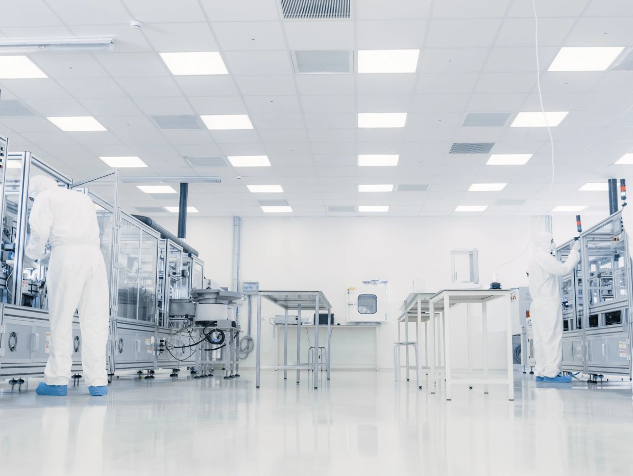Workers in cleanroom suits operating equipment in a sterile lab.