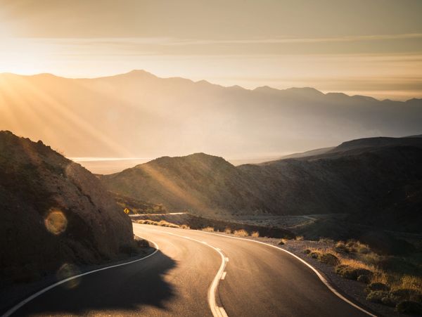 Sunlit winding road through mountainous landscape during golden hour.