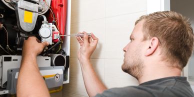 Technician repairing a boiler with a screwdriver indoors.