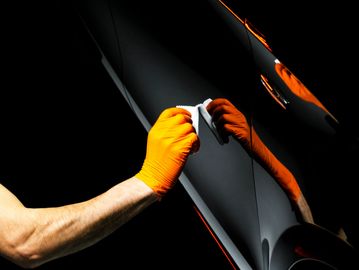 Person wearing orange gloves cleaning a car.