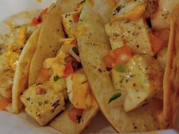 Three grilled fish tacos with diced tomatoes and herbs.