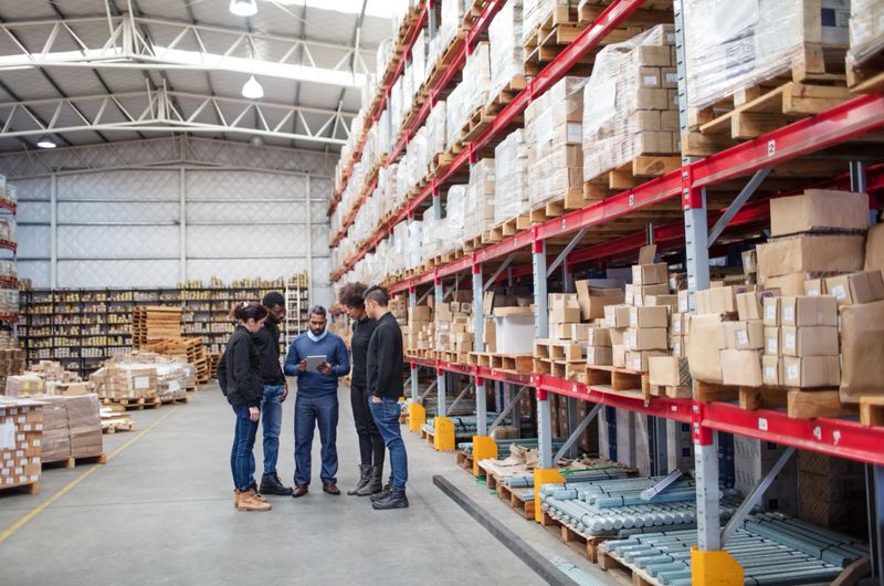 Mature manager with digital tablet discussing work with logistics team. Warehouse worker meeting over delivery schedule.