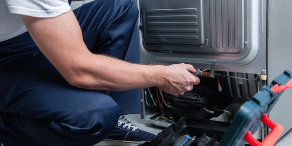 Technician repairing the back of a refrigerator with tools.
