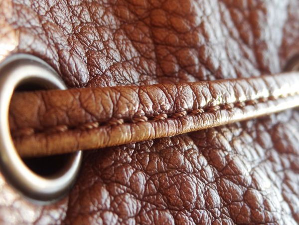 Upclose picture of brown textured leather with a leather-sown stitch through and eyelit