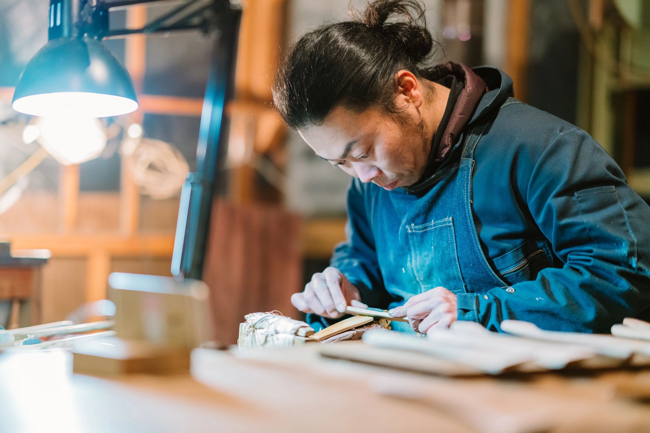 Man focused on woodworking under a bright lamp.