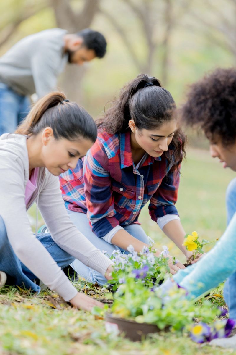 Diverse group of female friends work together to plant flowers during community beautification event.