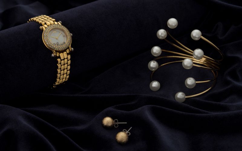 Golden wrist watch and bracelet with pearls and golden earrings pair on velvet fabric background