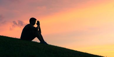 Silhouette of a person meditating on a hill during a colorful sunset.