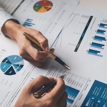 Two people analyzing financial charts and graphs with pens.
