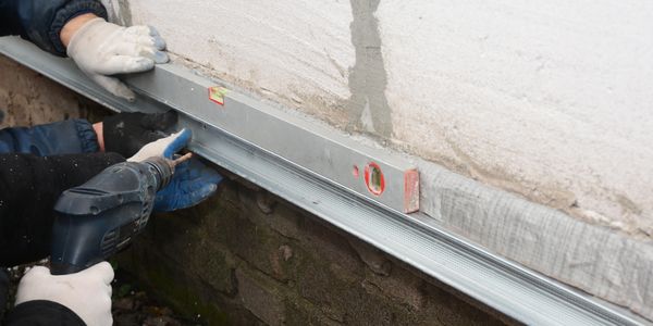 Two workers using a spirit level and electric drill on a wall.