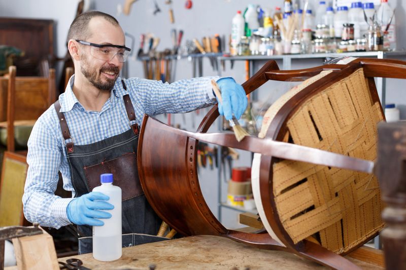 Concentrated professional restorer varnishing vintage chair in workshop