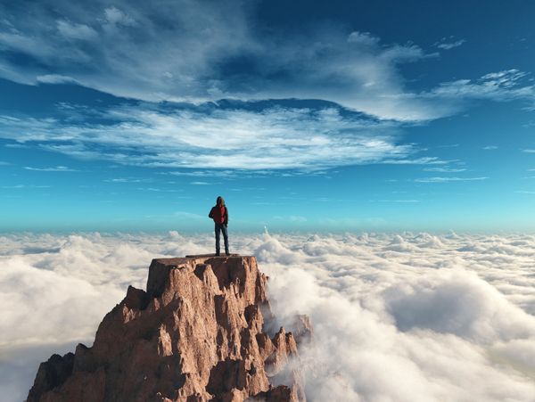 A lone hiker stands atop a rocky peak above the clouds under a vibrant blue sky.