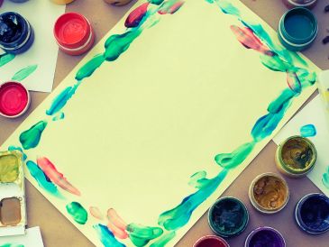 Colorful paint pots surround a paper with a painted border.