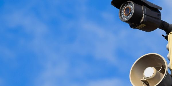 Surveillance camera and loudspeaker against a blue sky.