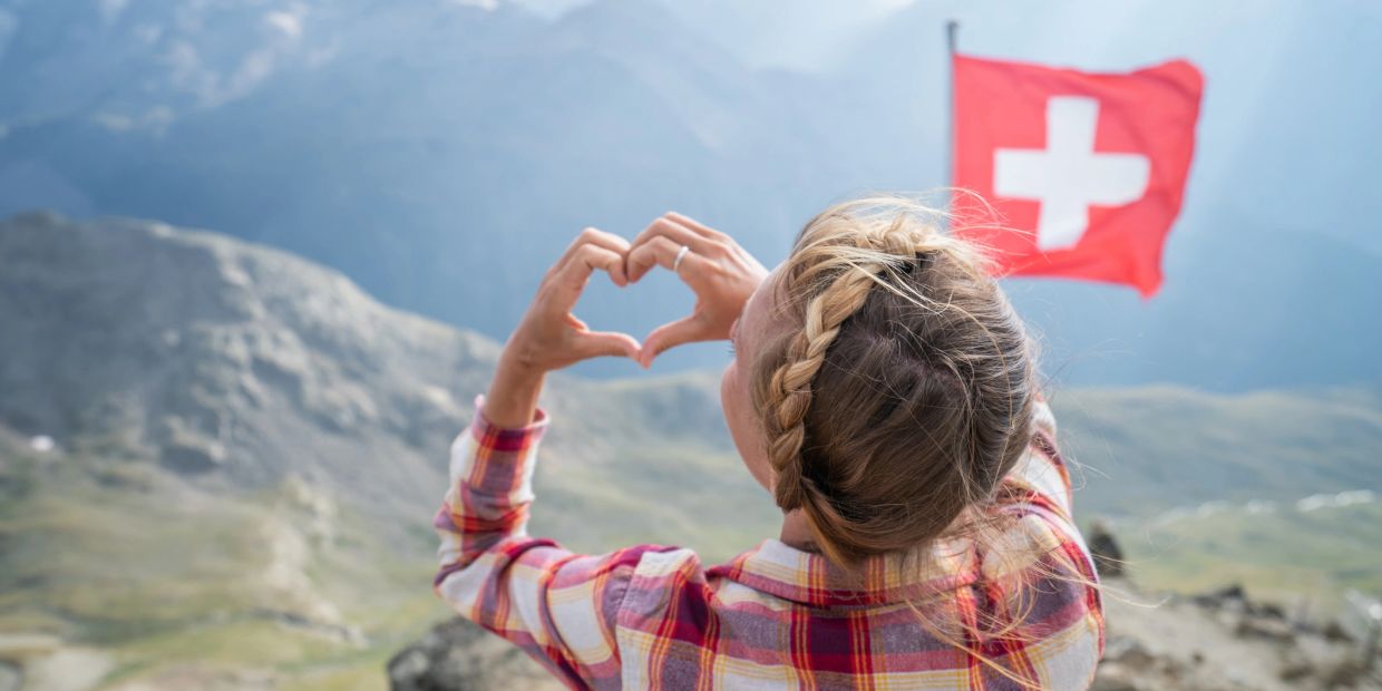 Woman making a heart shape with hands near a Swiss flag.