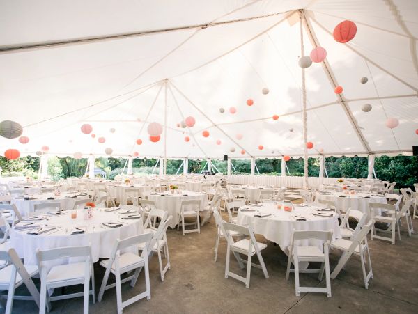 Decorated tent with round tables and white chairs for an event.