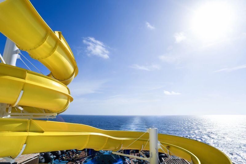 Yellow water slide at the rear of a cruise ship set against a blue sky.