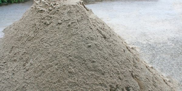 A large pile of sand on a gravel surface.