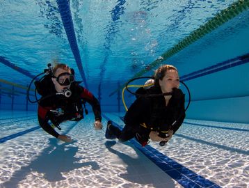 Two scuba divers practicing underwater in a swimming pool.