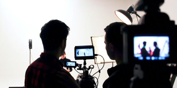 Two people filming a scene with professional cameras and lighting setup.