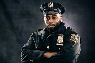 Confident police officer in uniform with arms crossed against dark background.