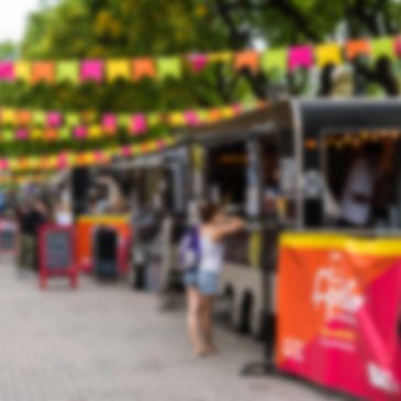 Colorful food trucks line a busy street festival with vibrant hanging banners.