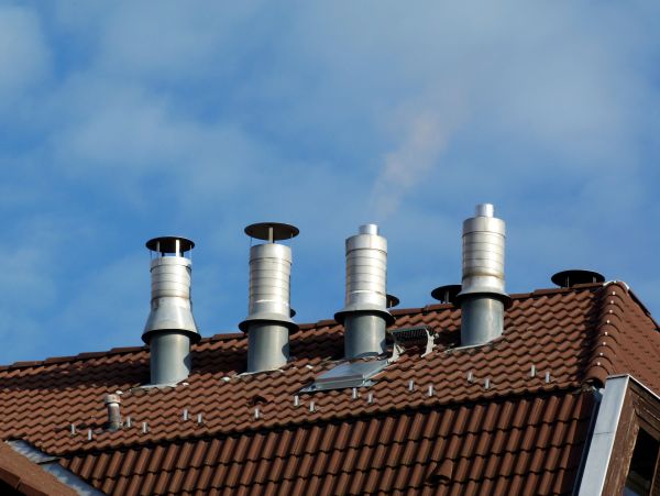 Metal chimneys on a tiled roof under blue sky.