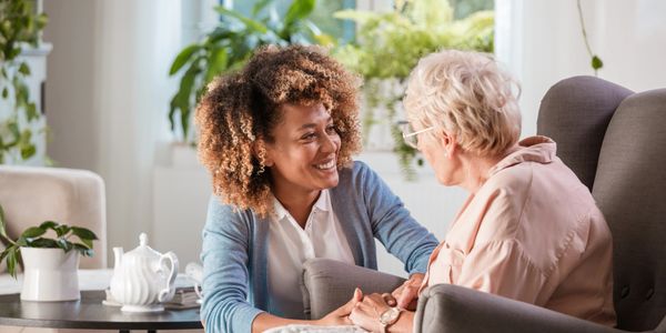 A young woman warmly talking to an elderly woman in a cozy living room.