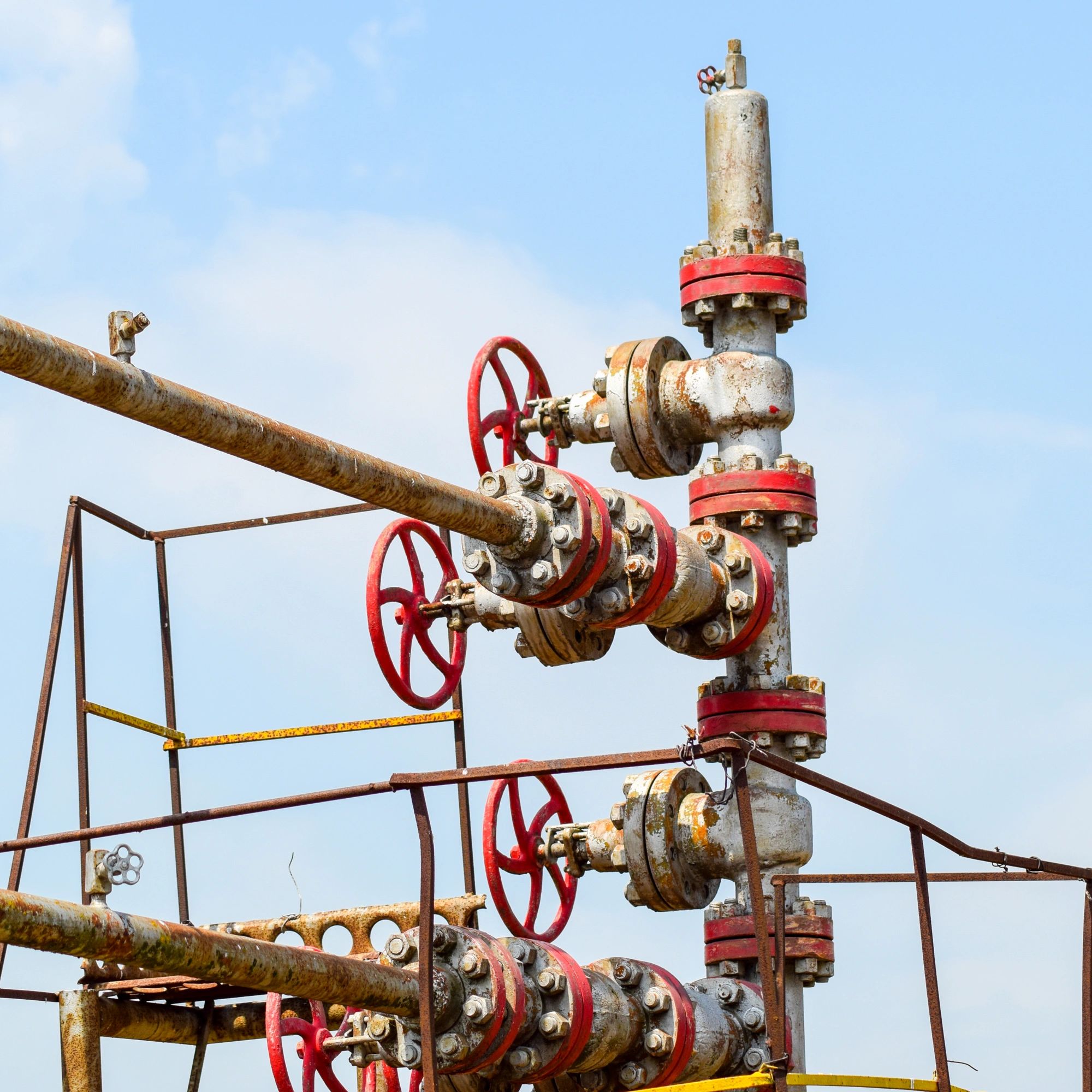 Rusty industrial pipes and red valves against a blue sky.