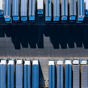 Aerial view of parked semi-trailer trucks casting long shadows on asphalt.