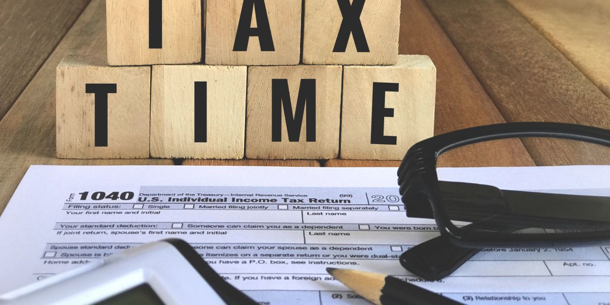 Wooden blocks spell out TAX TIME above a tax form, calculator, pencil, and glasses.