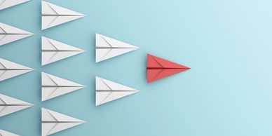 Red paper airplane leading white ones on a blue background.