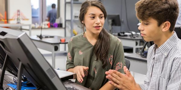 Two students collaborating on a project using a desktop computer in a modern classroom.