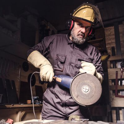 A man in protective gear using an angle grinder in a workshop.