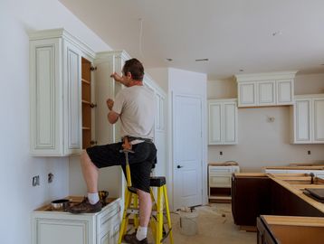 Man installing kitchen cabinets during renovation work.