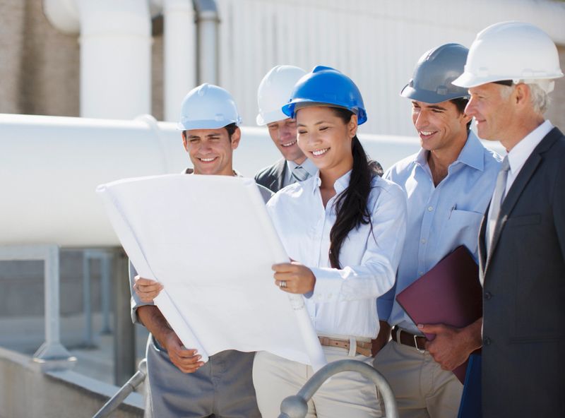 Business people in hard-hats reviewing blueprints outdoors