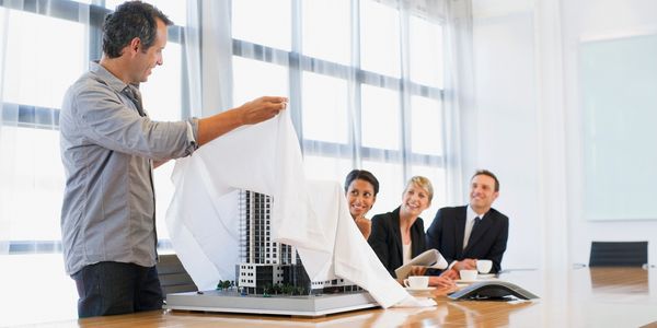 Man unveiling architectural model to colleagues in meeting.