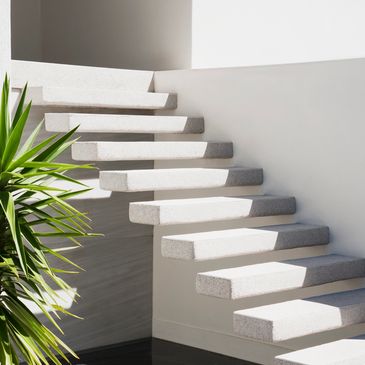 Escalera blanca flotante con luz natural y planta.