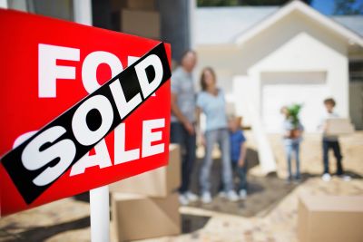 A sold sign in front of a new house with a family in the background.