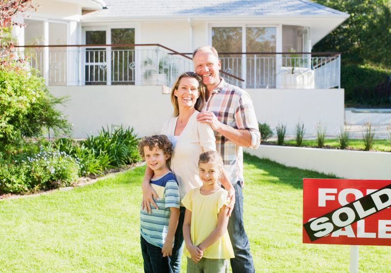 Family standing in front yard of new house next to sold sign
