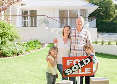 Happy family standing in front of their newly sold home with moving boxes.