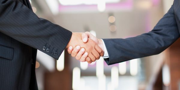 Two people in suits shaking hands in a professional setting.
