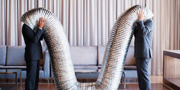 Two men in suits connected by a large metallic tube covering their heads.