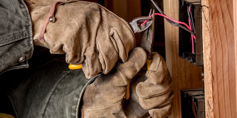 Electrician wearing gloves working on wiring inside a wooden wall.