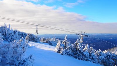 Snow-covered ski slope with chairlift and frosted trees under a partly cloudy sky.