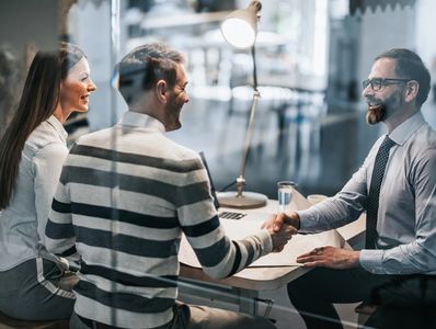 A couple shaking hands with a professional man in an office setting, showcasing trusted financial services.
