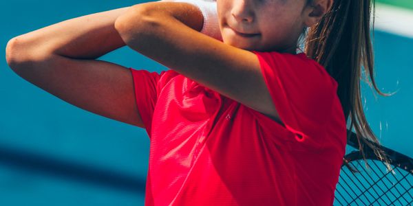 Young girl in a red shirt preparing to swing a tennis racket.